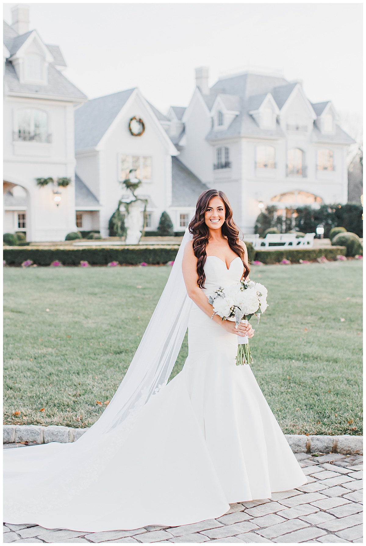 bride smiling with white floral bouquet in front of park chateau 