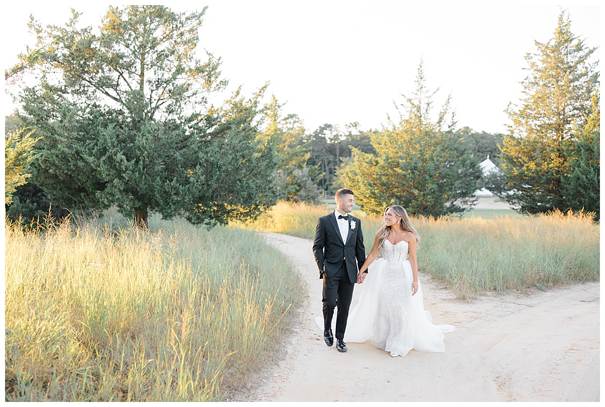 Bride and groom holding hands on the golf course with high grass during sunset at Renault Winery. 