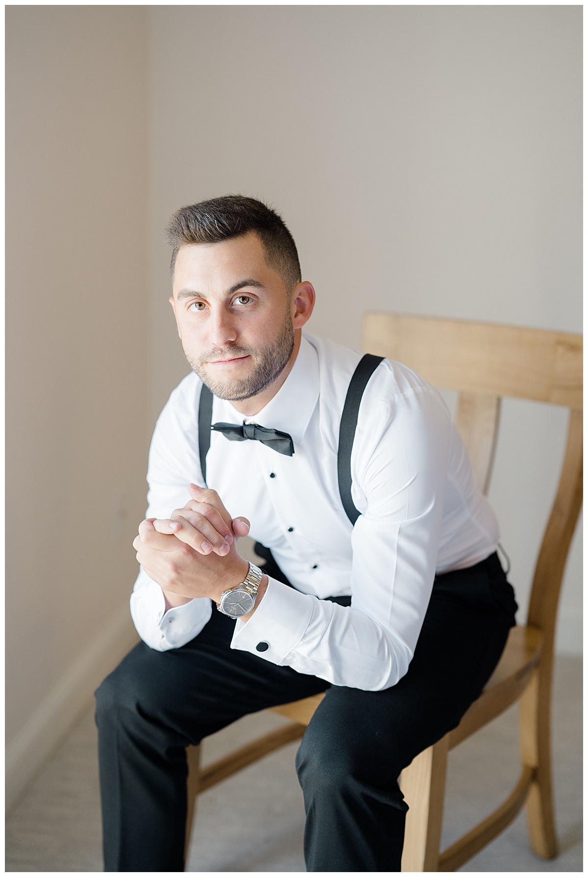 Groom with bowtie sitting down in chair for groom portraits. 