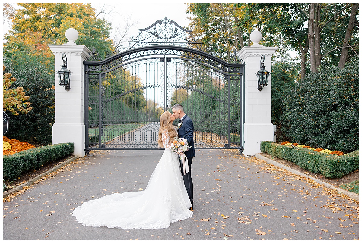 Bride and groom kissing in front of iron gates during the fall at Shadowbrook at Shrewsbury. 