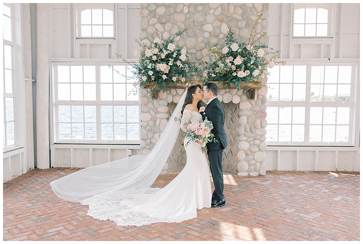 Bride and groom in the chapel with stone fireplace behind them as veil floats in the wind at Mallard Island Yacht Club. 