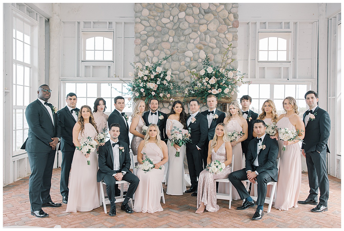 Large bridal party in blush and black tuxedos while sitting in the Chapel at Mallard Island Yacht Club. 