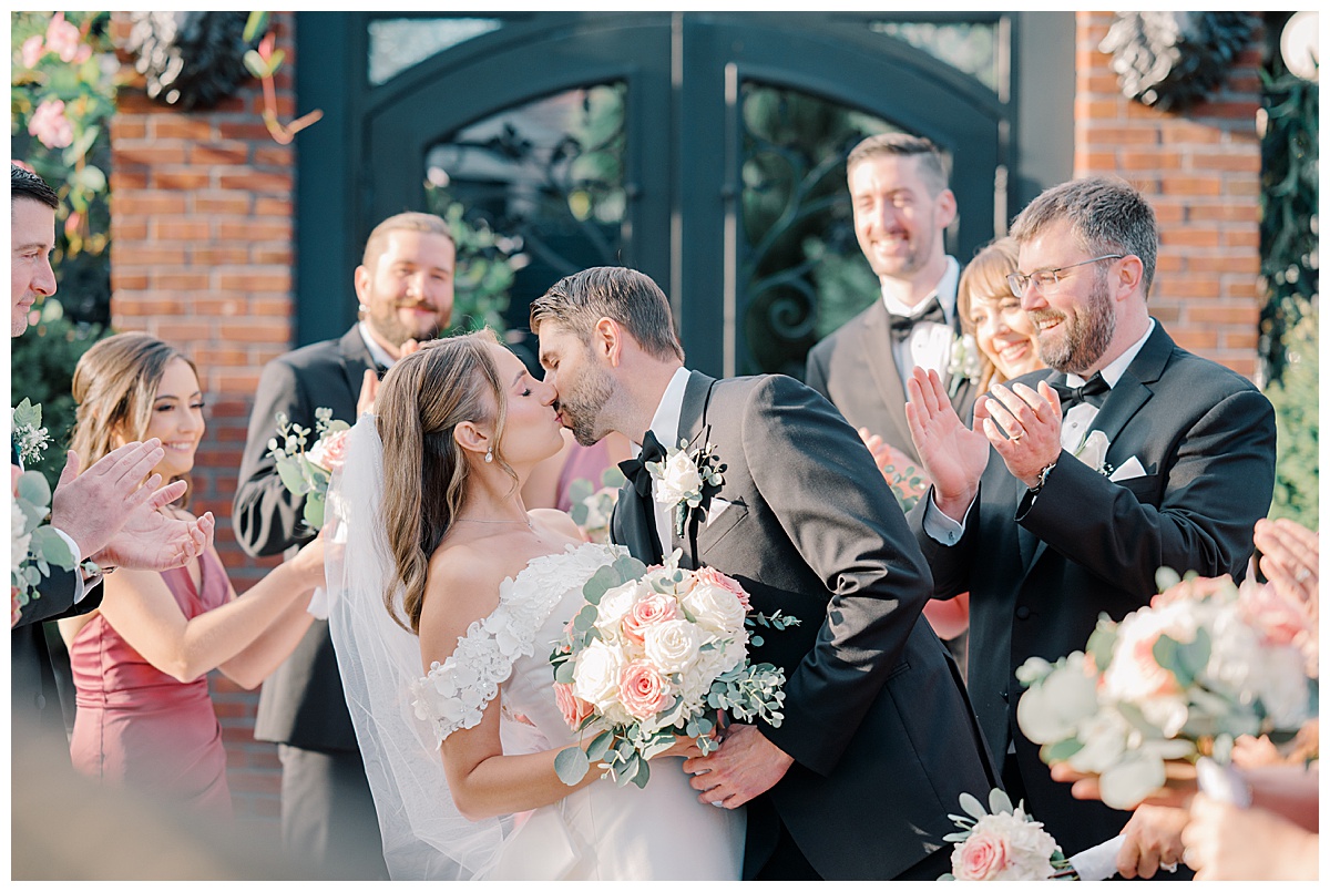 bride and groom kissing as bridal party claps and cheers