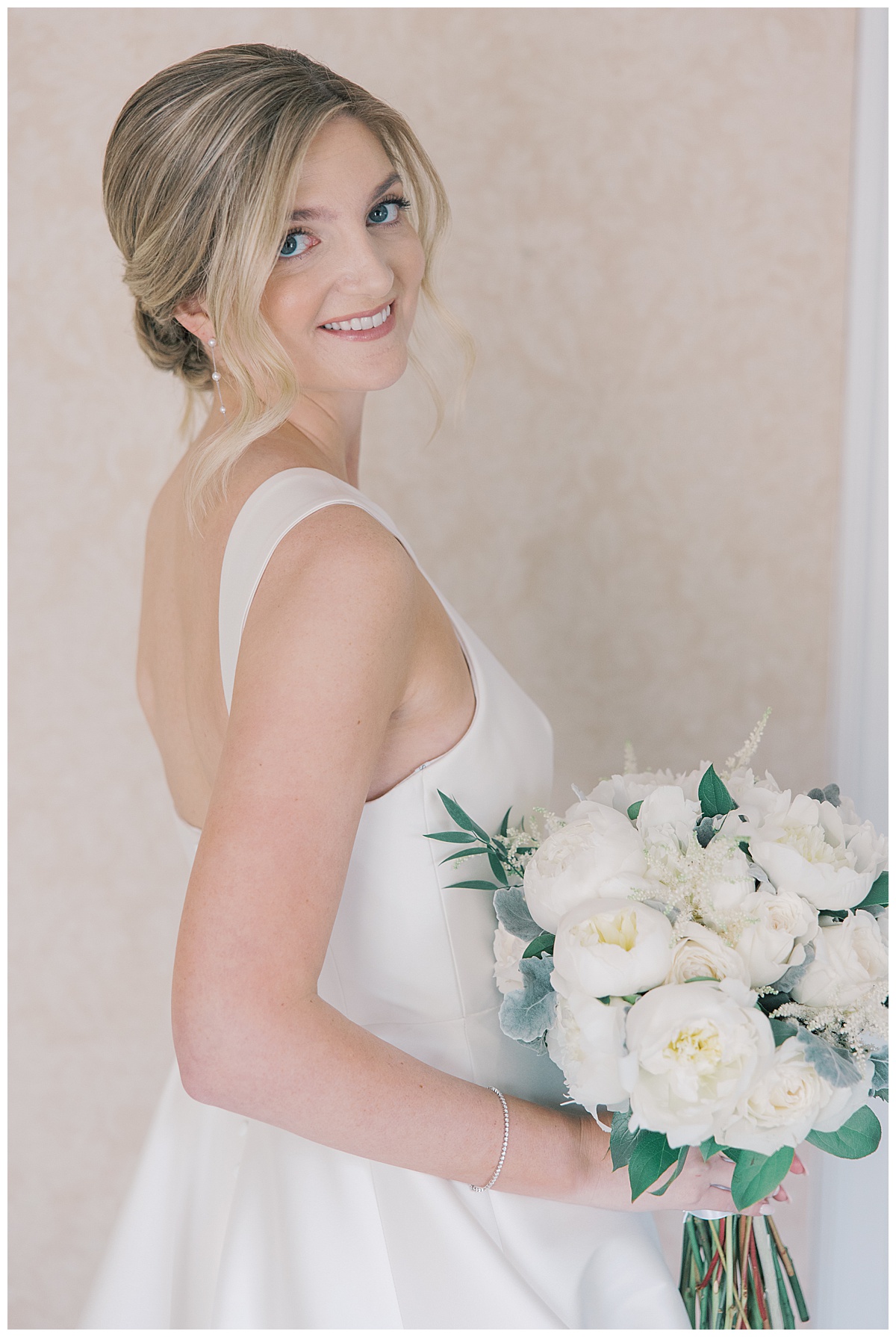 Bride with updo looking over shoulder with white peonies on wedding day.