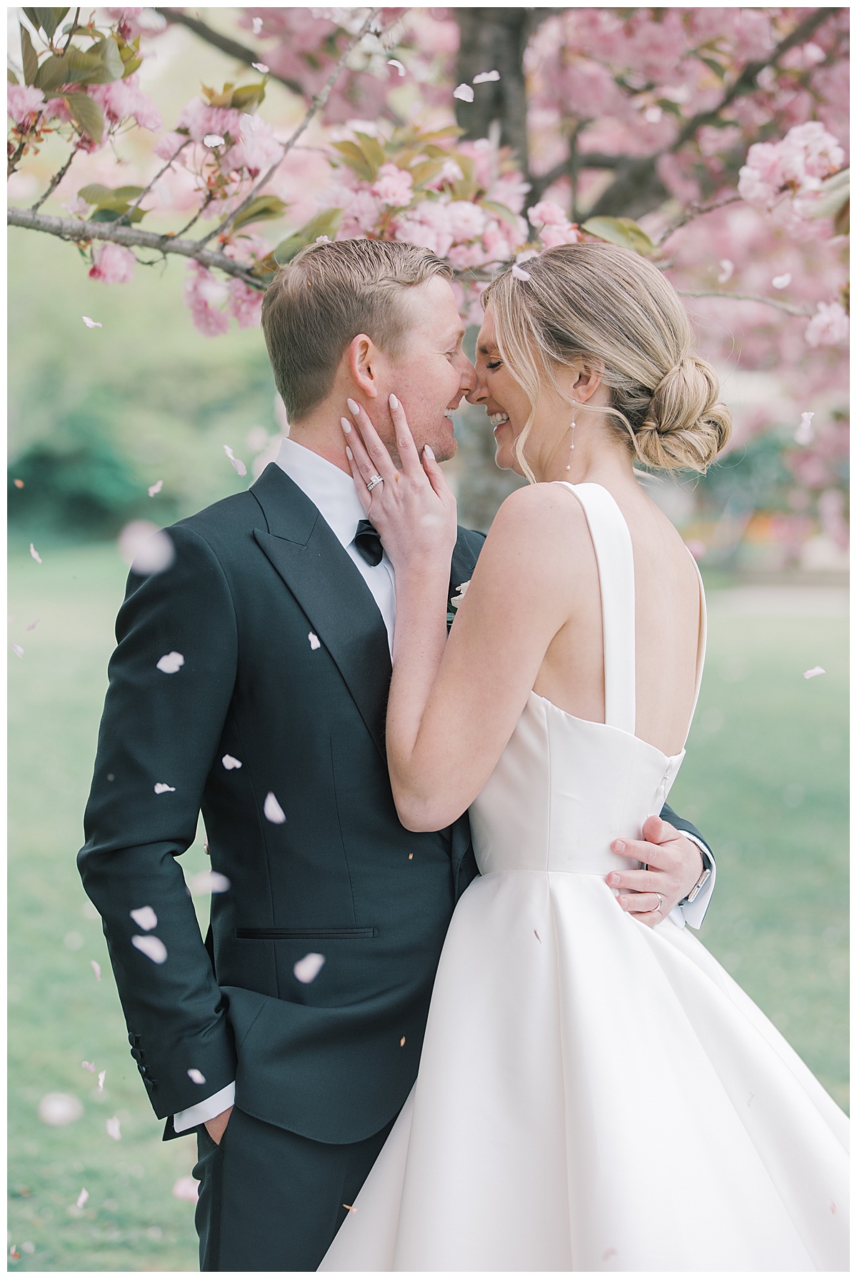 Bride and groom laugh at each other as cherry blossoms fall in front of them at The Mill Lakeside Manor. 