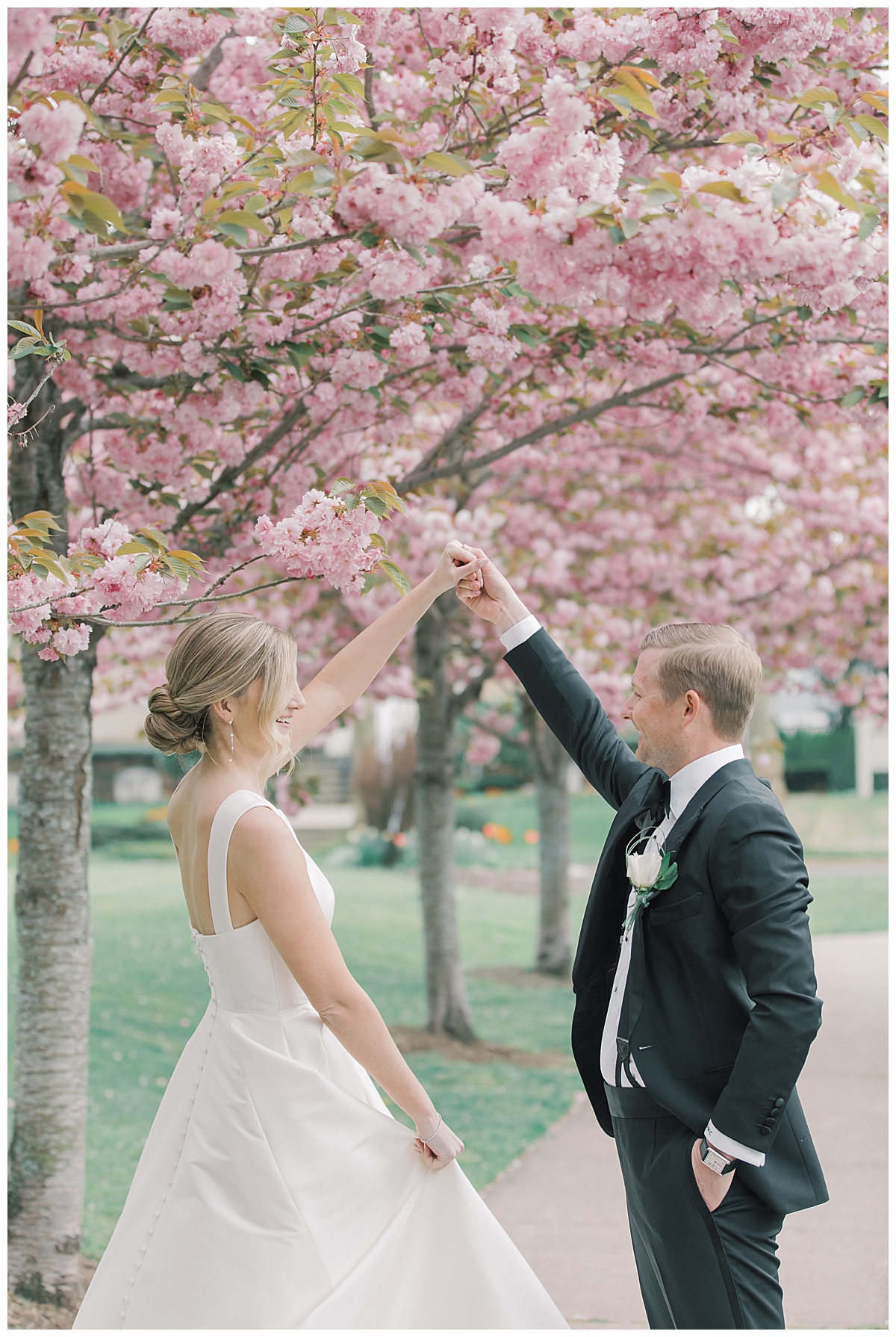 Groom twirls bride under cherry blossoms at The Mill Lakeside Manor. 