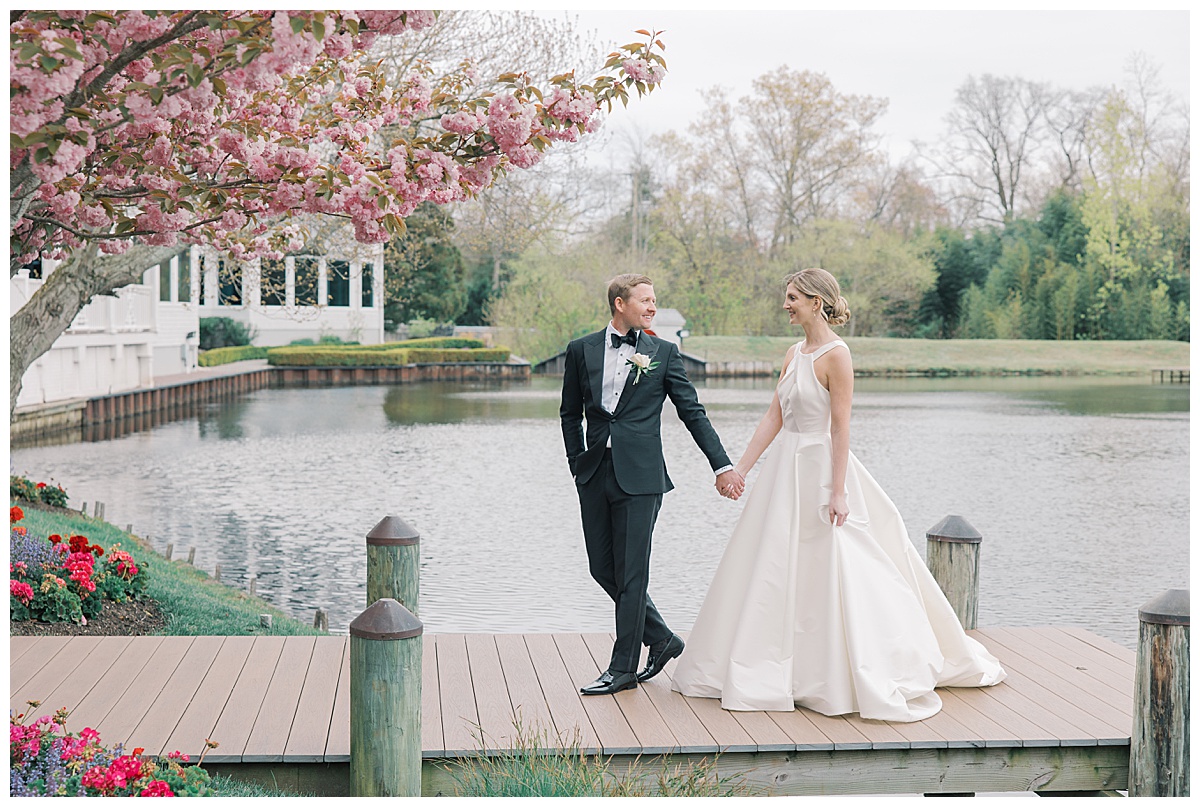 Groom leads bride off the dock with the lake behind them at The Mill Lakeside Manor. 