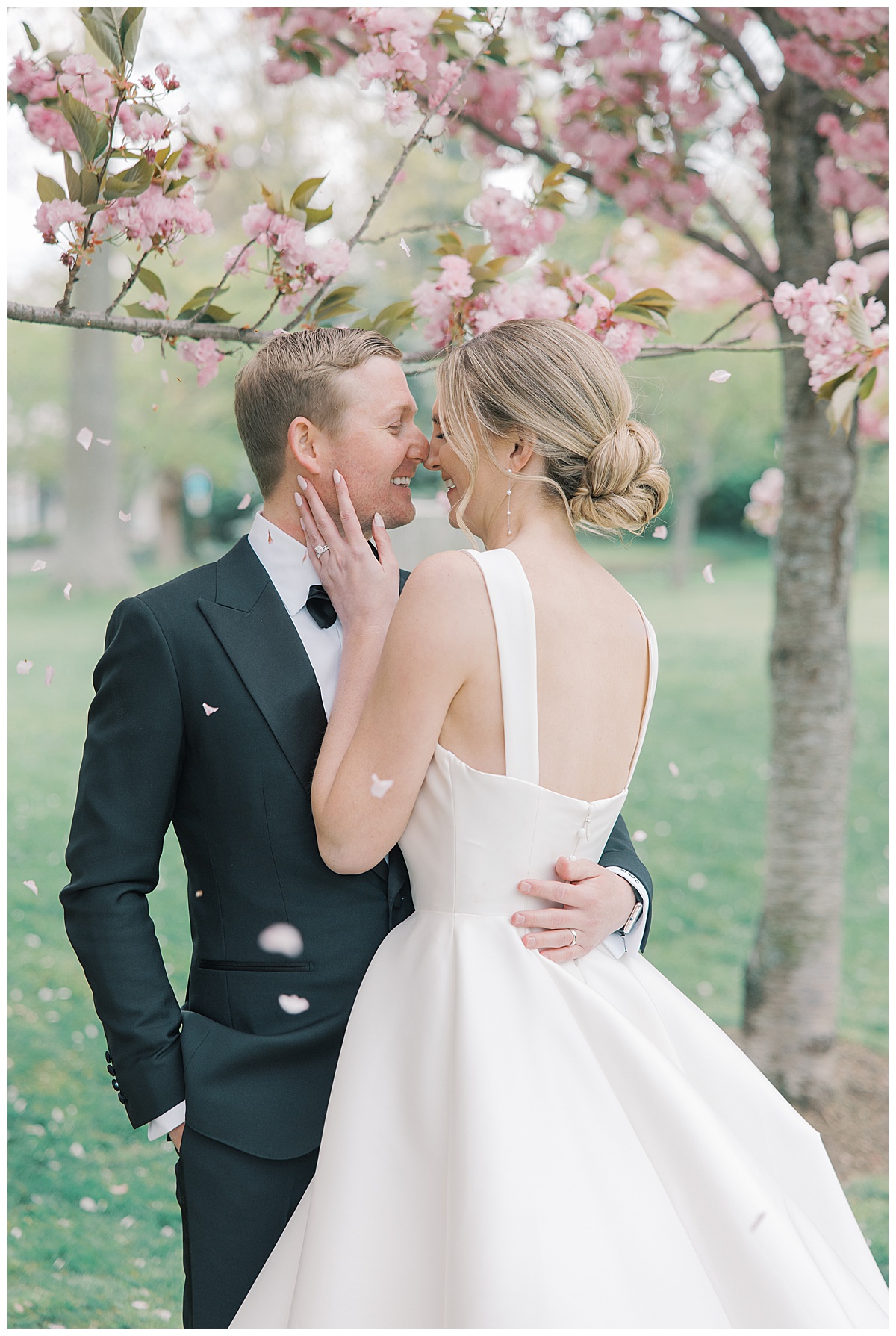 Cherry blossoms fall on bride and groom as they share a laugh with each other at The Mill Lakeside Manor. 