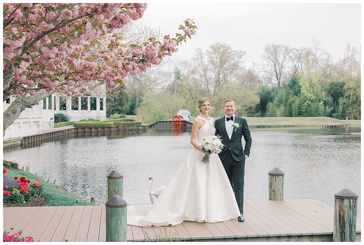Bride and groom on the dock at The Mill Lakeside Manor while swan swims behind them. 