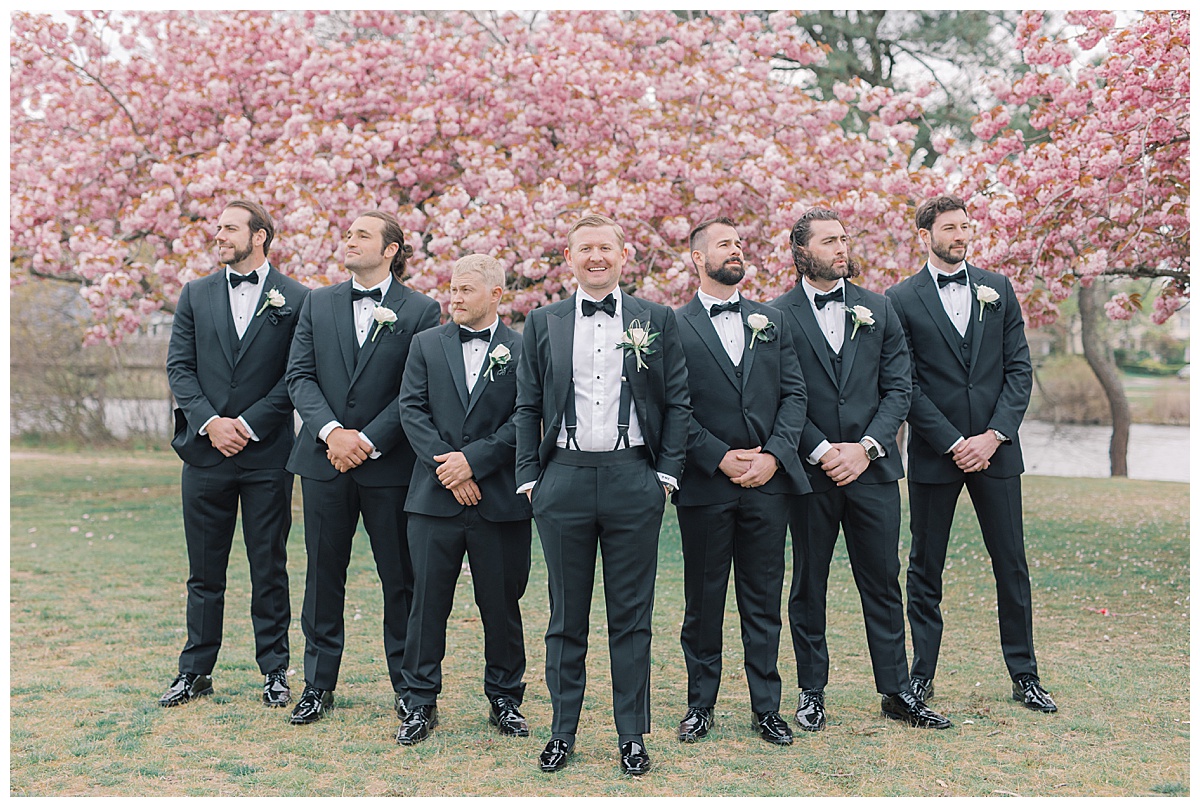 Groomsmen in black tuxedos with cherry blossoms behind them. 