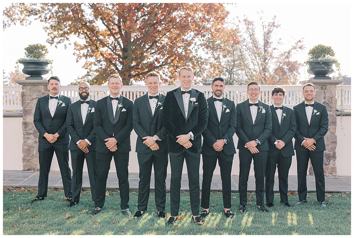 Groomsmen in black tuxedos as the sun sets behind them at The Ryland Inn. 