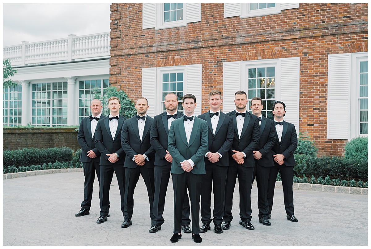 groomsmen in black tuxedos and groom standing out with a hunter green jacket 