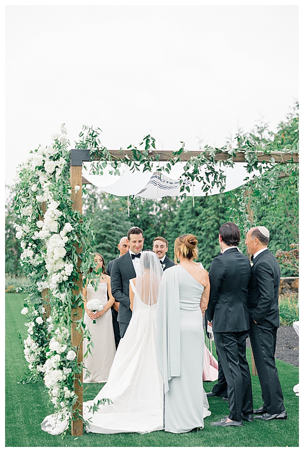 Hannah and Jake exchanging vows beneath a stunning white and green chuppah