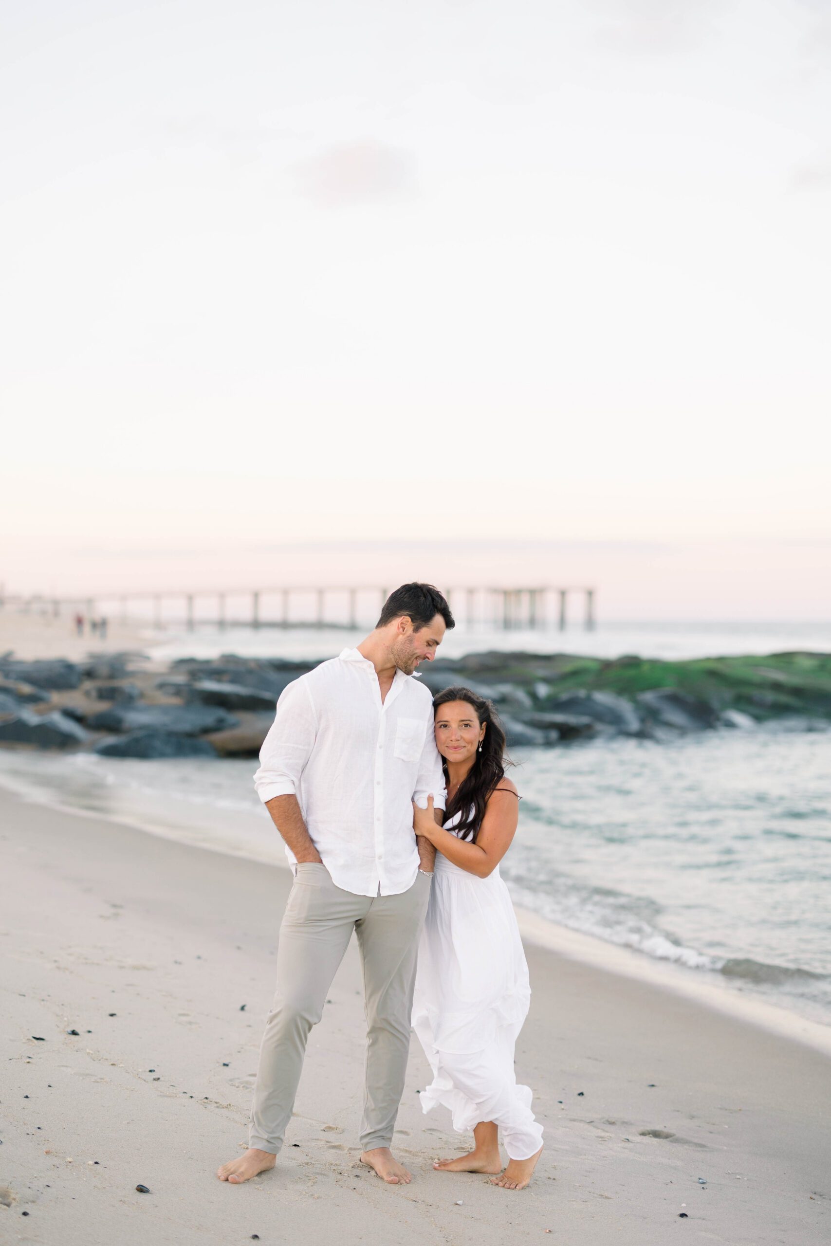 NJ beach engagement couple in white dress and khaki pants walking along Spring Lake shoreline